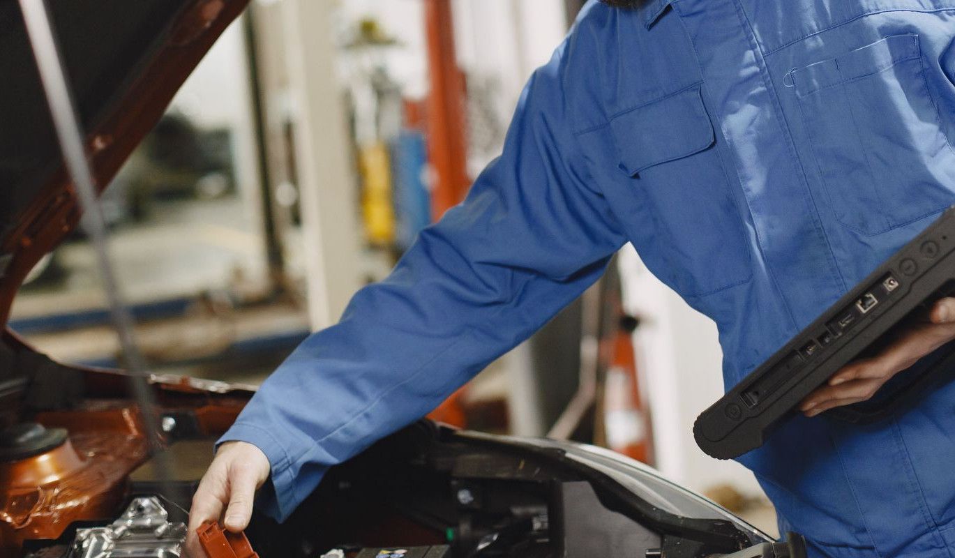 An auto mechanic in blue coveralls inspecting a car's engine in a garage.